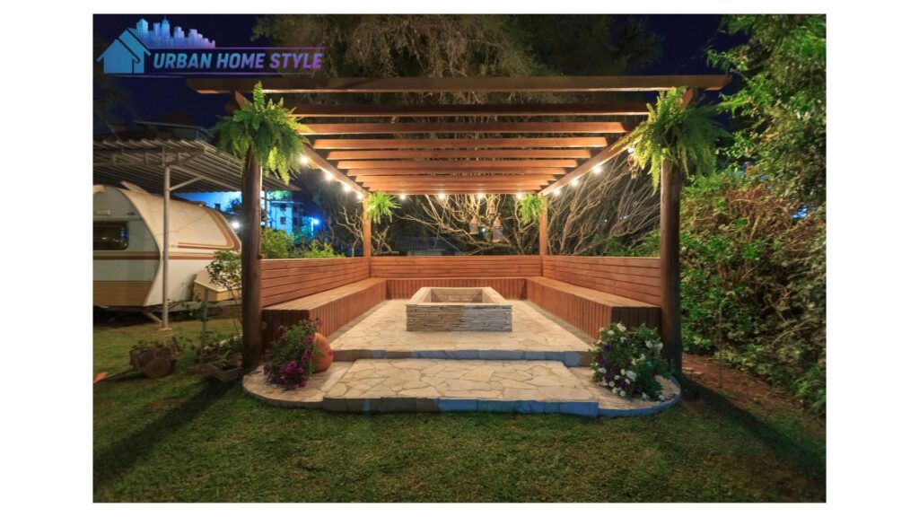 A backyard fire pit area covered by a timber pergola draped with fairy lights and climbing jasmine, with rattan outdoor furniture arranged around the fire on a warm summer evening.
